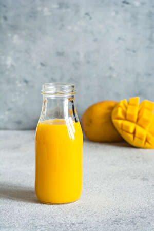 Fresh mango juice in a glass glass with mango slice on a gray background. Exotic drink, copy space. Trending colors of the yearの写真素材