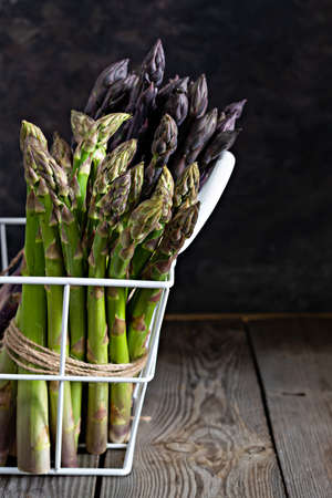 Raw purple, green asparagus in a basket on a dark wooden background. Raw food concept, place for copy space.の写真素材