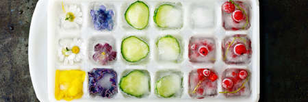 Multicolored frozen ice cubes with fruits, flowers and vegetables on a dark background in the form of ice.の写真素材