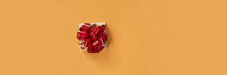 Banner with a Gift box, with a bright shiny red bow on a bright orange (yellow) background. Present for birthday, christmas, new year. Festive concept.の写真素材
