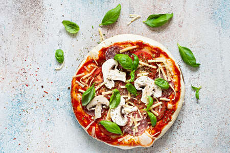 Cooking Italian pizza with tomato sauce, fresh tomatoes, cheese, mushrooms, salami slices and basil . Fresh food cooking concept at home. Semi-finished product, raw dough, step by step cooking.の写真素材