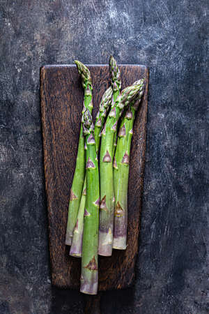 Green asparagus on a wooden cutting board on a dark background. Raw food concept, place for copy space.の写真素材