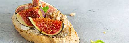 Crispy bruschetta (toast) with soft ricotta, ripe figs, walnuts and pine nuts, mint and honey on a light background.の写真素材