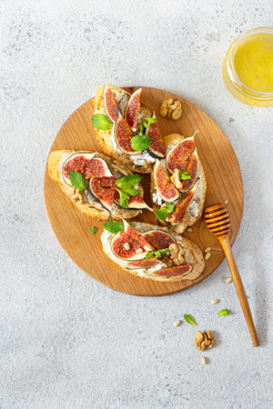 Crispy bruschetta (toast) with soft ricotta, ripe figs, walnuts and pine nuts, mint and honey on a...