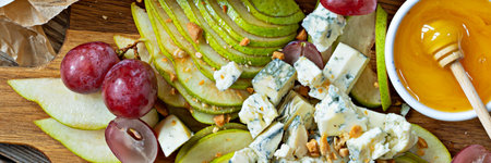 Sliced Blue cheese, dor blue or roquefort and fruits (grapes, pears), nuts and honey on a board. Exquisite appetizer for wine. fruity cheese plate.の写真素材