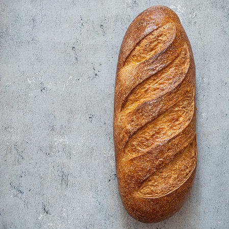 Freshly baked loaf on a light gray (blue) background. Traditional fresh bread in the form of a long...