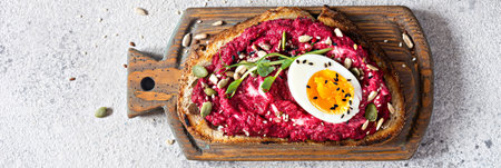Whole grain toast with beetroot hummus, seeds, egg and microgreens (sprouted pea sprouts) on wooden board on a light gray background. The concept of healthy eating. Viva magentaの写真素材
