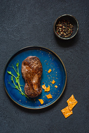 Grilled spiced marbled beef steak with microgreens and crispbread on black background. The shape of the steak is light bulb. Food energy concept for human, top view, minimalism.の写真素材