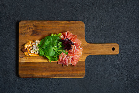 Salad of jamon (prosciutto) spinach and lettuce with crispy savory bread, nuts, microgreens on black background. Flat lay of food in form of light bulb on board. food energy conceptの写真素材
