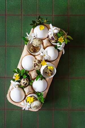 Easter eggs in a decorative stand decorated with flowers and greenery on green background. Festive Easter concept, dinner table decoration.の写真素材