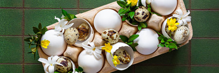 Easter eggs in a decorative stand decorated with flowers and greenery on green background. Festive Easter concept, dinner table decoration.の写真素材
