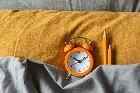 Alarm clock in bed on colored textiles. The concept of awakening, work time, training (studying), back to school. Get up, wake up and live, distance learning. Bedtime, copy space.の写真素材