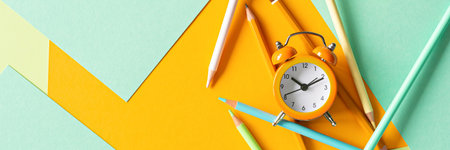 Back to school, education and work concept. Stationery for learning (study) and alarm clock on mint yellow background. View from above, top view. Wake up time.の写真素材