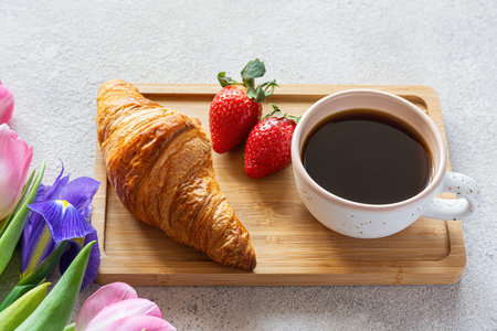 Beautiful breakfast with cup of coffee, fresh croissants, strawberries on tray, bouquet of tulips as...