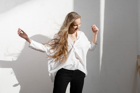 Beautiful fresh blonde model in white shirt and black trousers. Shadows on backgroundの写真素材