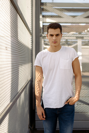 Beautiful caucasian man in white t-shirt and blue jeans stay on the streetの写真素材