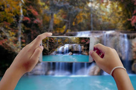 Travel concept, take photography waterfall in autumn forest at Erawan waterfall National park Kanchanaburi Thailand by phone