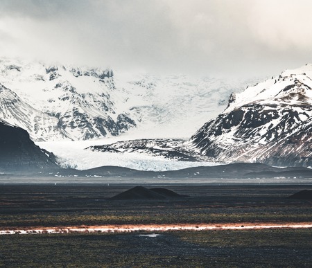Road leading towards huge glacier and mountains in Iceland Vatnajokull glacier aerial drone image with street highway and clouds and blue sky. Dramatic winter scene of Vatnajokull National Park, Iceland, Europe. Beauty of nature concept background.