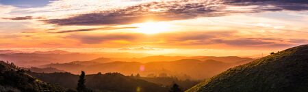 Sunlight bursting through the clouds and illuminating the hills and valleys of Santa Cruz mountains; clouds covering the sky and the Pacific Ocean; San Francisco bay area, California