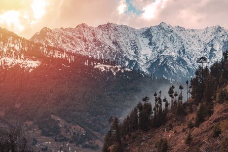 Landscape of mountain range covered with snow in Manali during summers, captured during the sunset with mist and fog